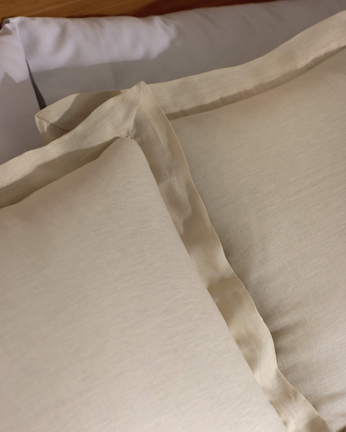 Close-up of two Cozy Earth Linen Shams in beige with subtle texture and flange edges, arranged neatly on a matching bed sheet. The bedding looks soft and inviting.|Color:Flax
