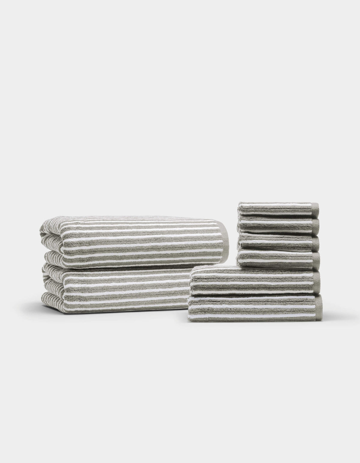 Two neatly arranged stacks of the Cozy Earth Ribbed Terry Bath Towel Set are displayed on a plain white background—one larger stack featuring bath towels, and a smaller stack showcasing hand towels and washcloths.|Color:Dew Stripe