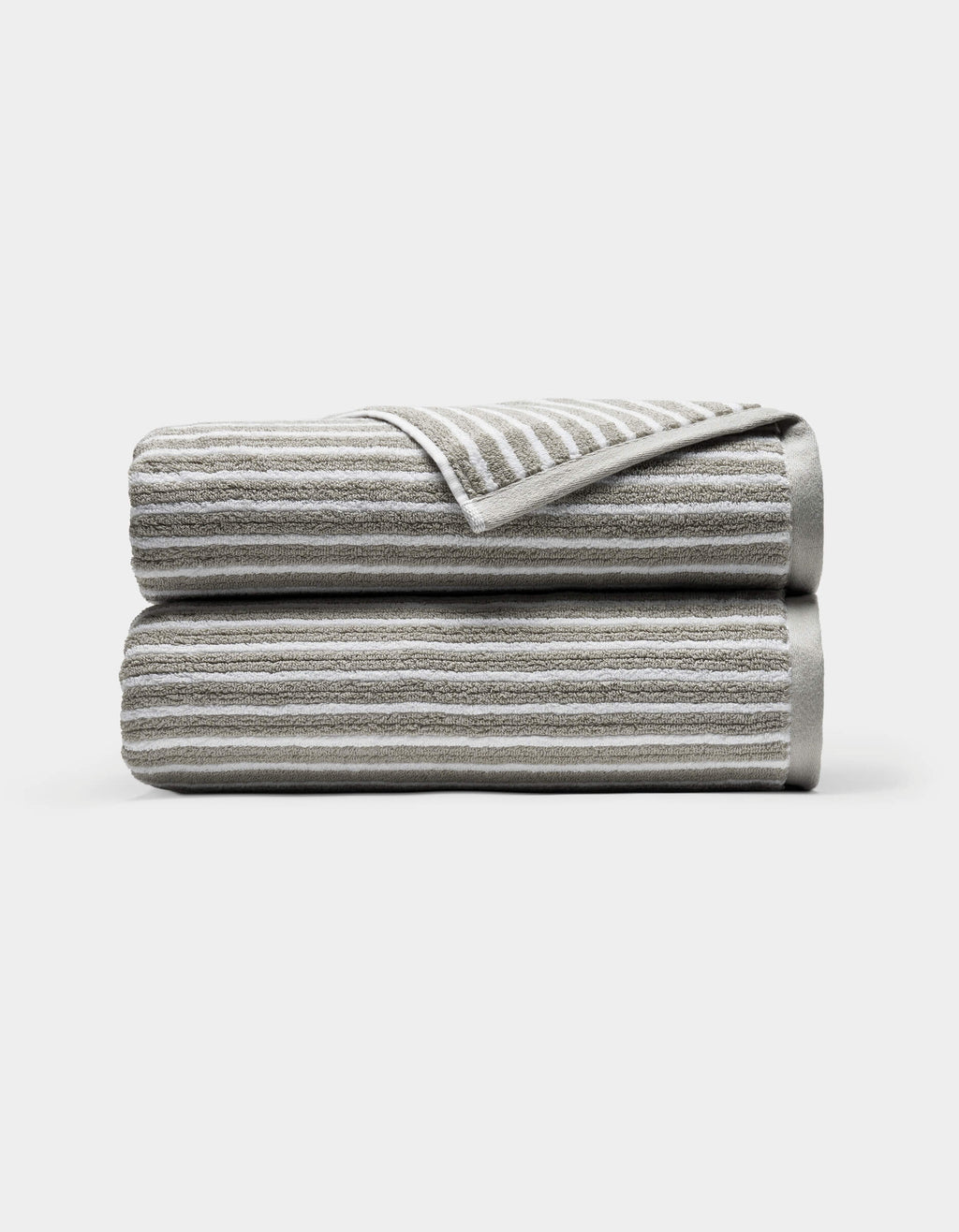 Two neatly folded Ribbed Terry Bath Towels by Cozy Earth, light gray with horizontal white stripes, stacked atop each other against a plain white background. A corner of the top towel is turned over, revealing the underside.|Color:Dew Stripe