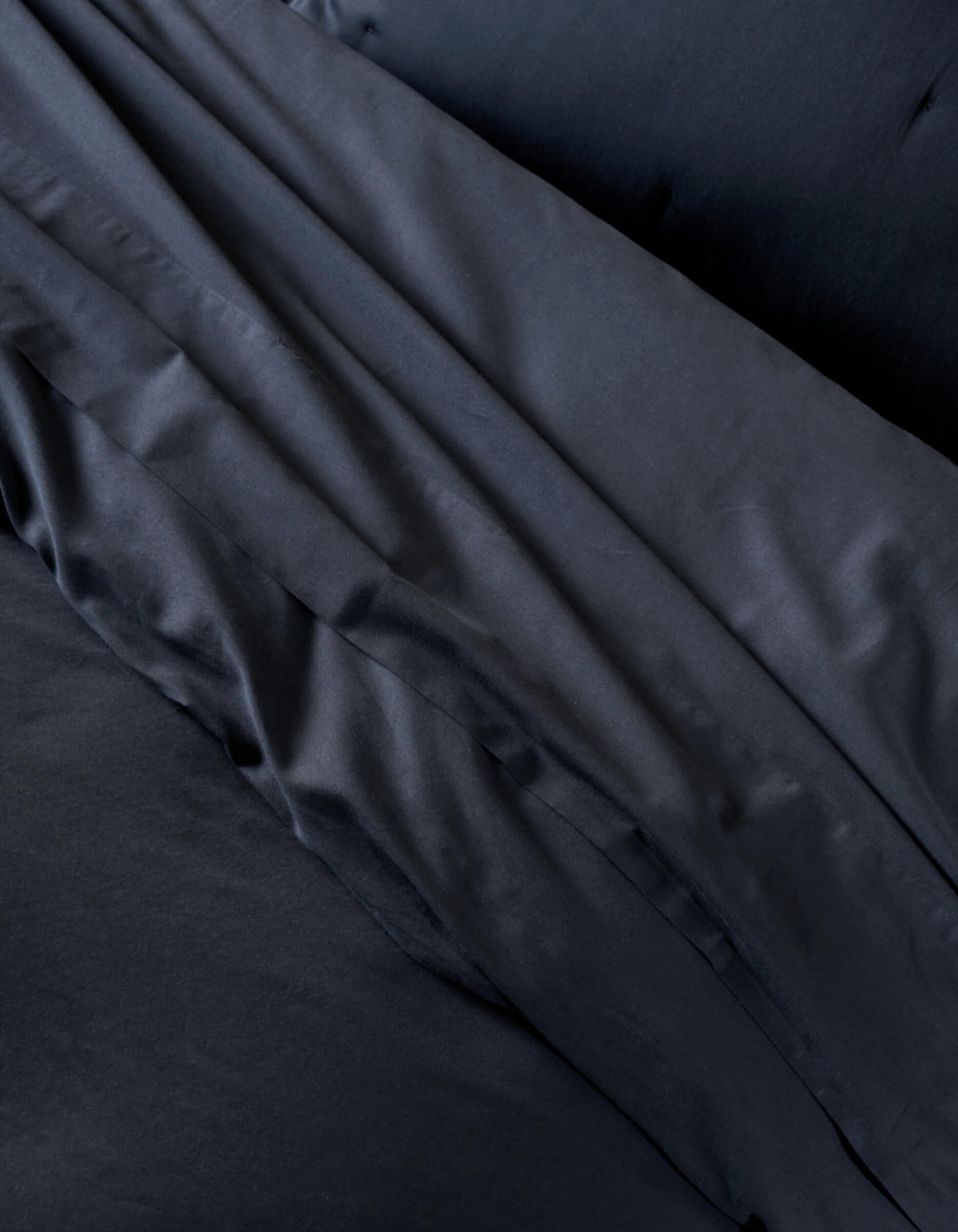 A close-up of the Cozy Earth Soft-Wash Cotton Duvet Cover shows neatly arranged black bedding and pillowcases, highlighting the smooth, slightly shiny fabric with gentle folds and creases.|Color:Eclipse