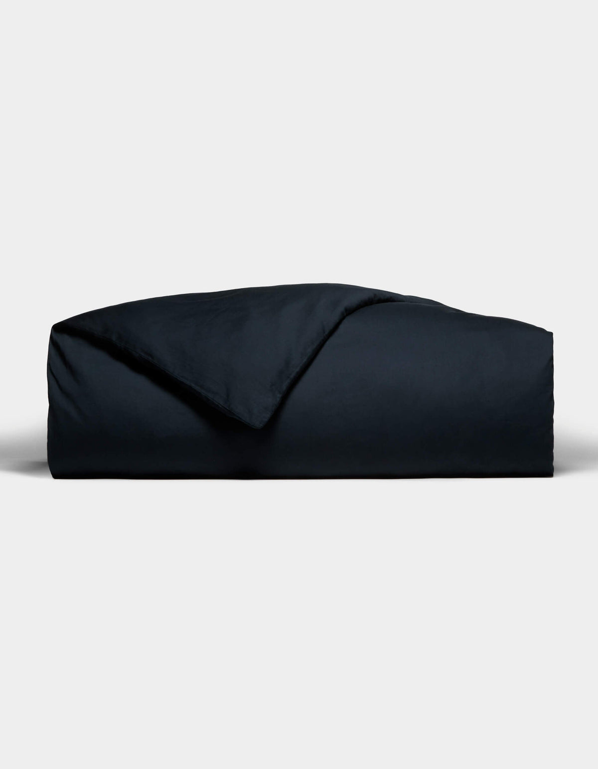 The Cozy Earth Soft-Wash Cotton Duvet Cover, in a dark hue, is neatly folded with one corner flipped to reveal its smooth texture, set against a plain light gray background.|Color:Eclipse