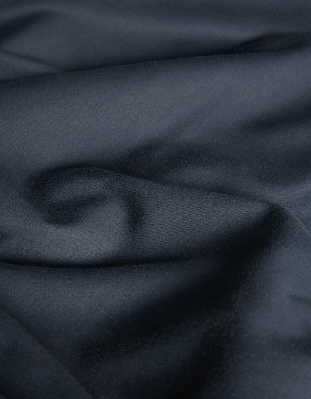 A close-up of Cozy Earth's Soft-Wash Cotton Flat Sheet reveals dark, smooth cotton with subtle folds and a soft, slightly glossy texture, creating a rich and elegant look.|Color:Eclipse