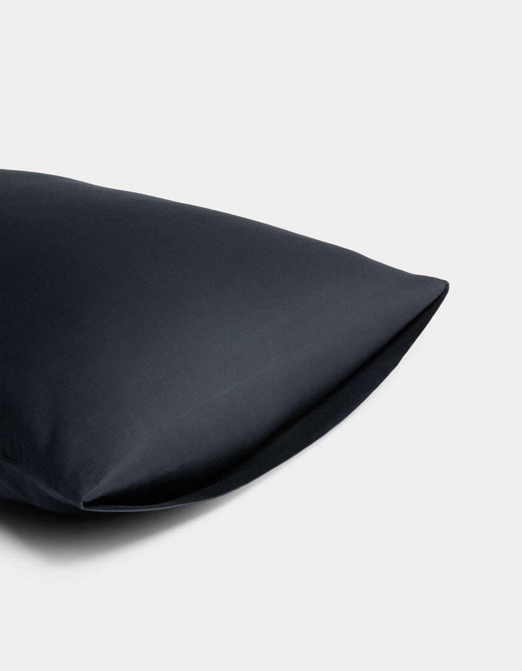 A close-up showcases the Soft-Wash Cotton Pillowcase by Cozy Earth in black, made from smooth fabric, set against a plain light gray background. Only part of the pillowcase appears on the left side of the image.|Color:Eclipse