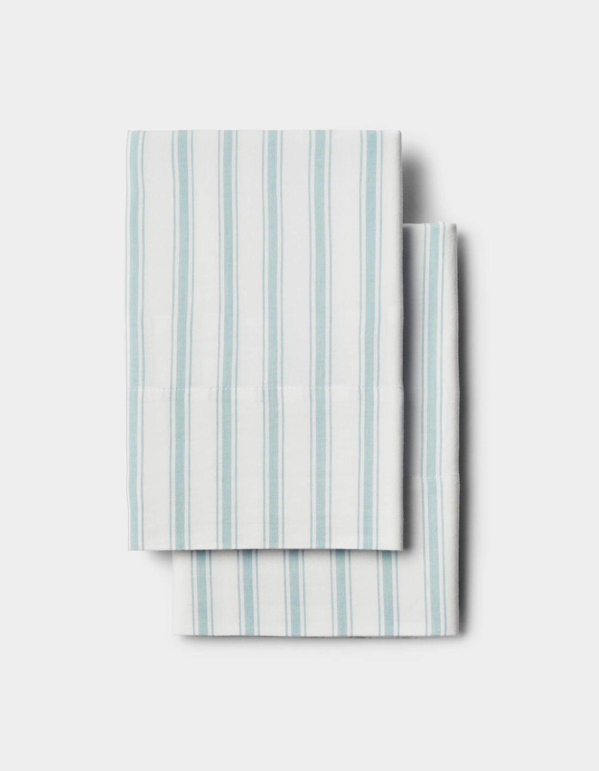 Two Soft-Wash Cotton Pillowcases by Cozy Earth, white with vertical light blue stripes, neatly folded and stacked on a plain light background.|Color:River and Sea Salt Stripe