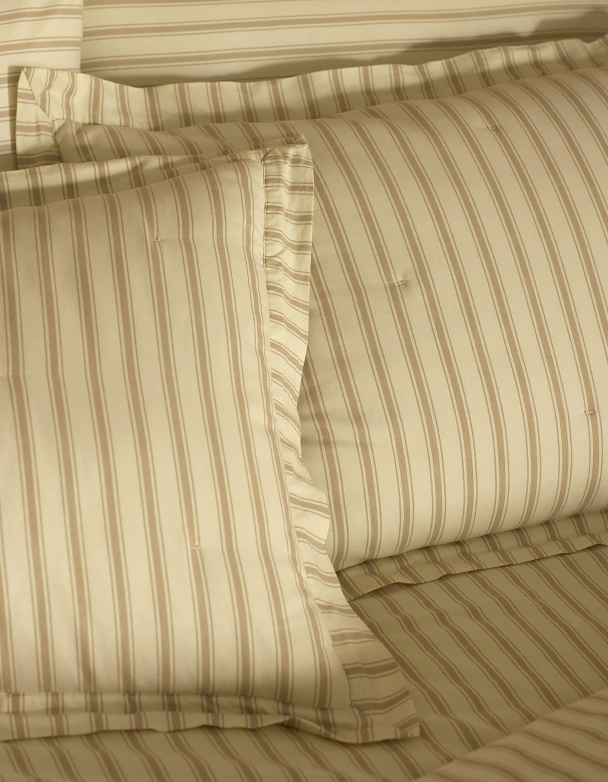 Close-up of a neatly made bed featuring Cozy Earth Soft-Wash Cotton Quilted Shams, showcasing smooth, soft fabric and subtle beige and light brown stripes on pillows and sheets for a cozy look.|Color:Coconut and Sandalwood Stripe