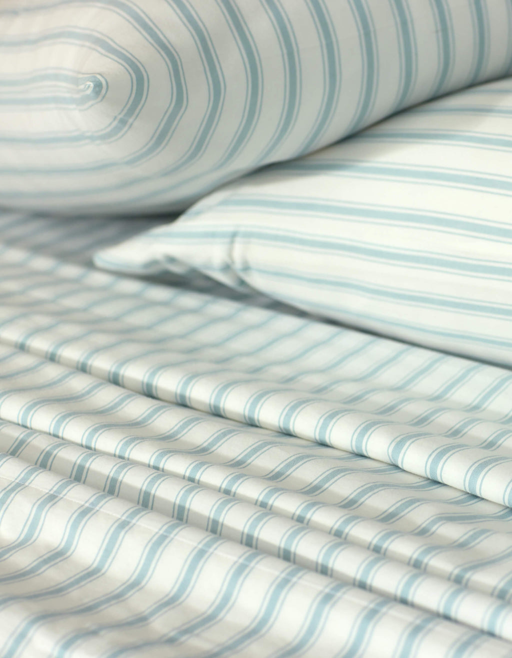 Close-up of a neatly made bed showcasing the Cozy Earth Soft-Wash Cotton Sheet Set, including a pillow, fitted sheet, and flat sheet in a light blue and white striped pattern. The smooth fabric looks exceptionally soft.|Color:River and Sea Salt Stripe