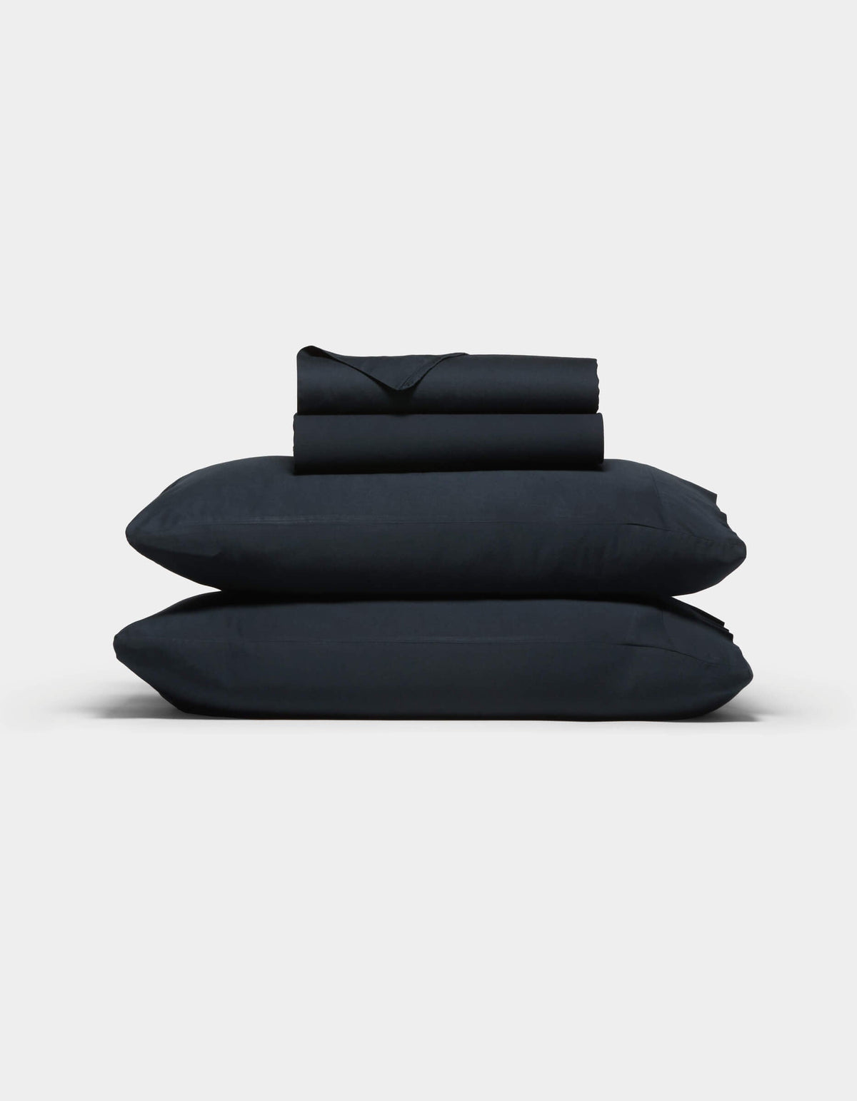 The Cozy Earth Soft-Wash Cotton Sheet Set, in dark navy blue, features two stacked pillows and folded sheets neatly arranged against a plain light gray background.|Color:Eclipse
