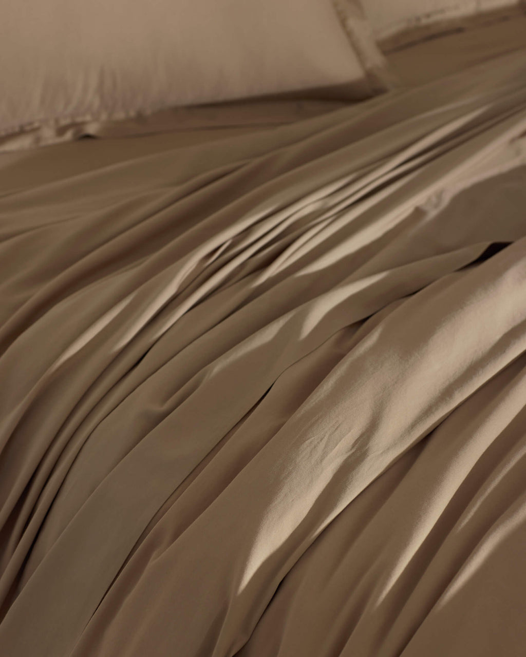 The Cozy Earth Soft-Wash Cotton Duvet Cover in brown is spread over the bed, creating gentle folds and shadows. Its smooth surface looks inviting, with matching pillowcases partially visible in the background.|Color:Sandalwood
