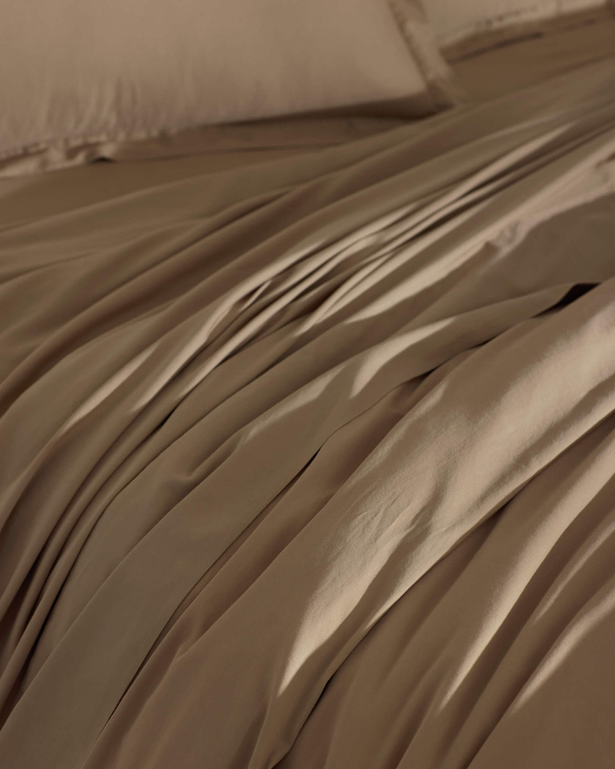 The Cozy Earth Soft-Wash Cotton Duvet Cover in brown is spread over the bed, creating gentle folds and shadows. Its smooth surface looks inviting, with matching pillowcases partially visible in the background.|Color:Sandalwood
