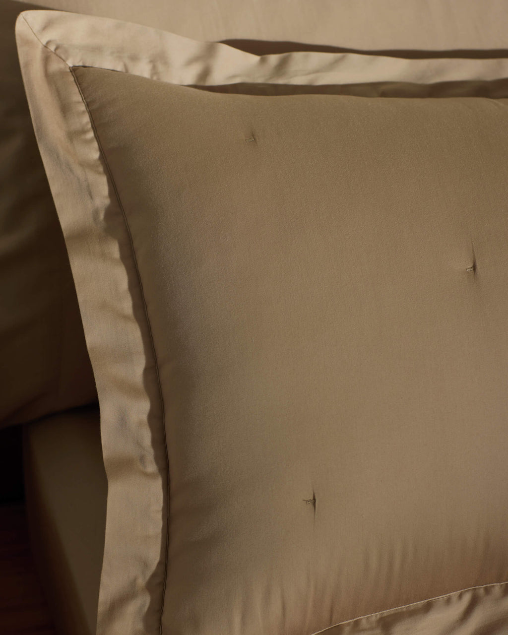 A close-up of a neatly made bed featuring Cozy Earth Soft-Wash Cotton Quilted Shams in beige, showcasing their smooth quilted texture and subtle tufting, complemented by matching beige bedding.|Color:Sandalwood