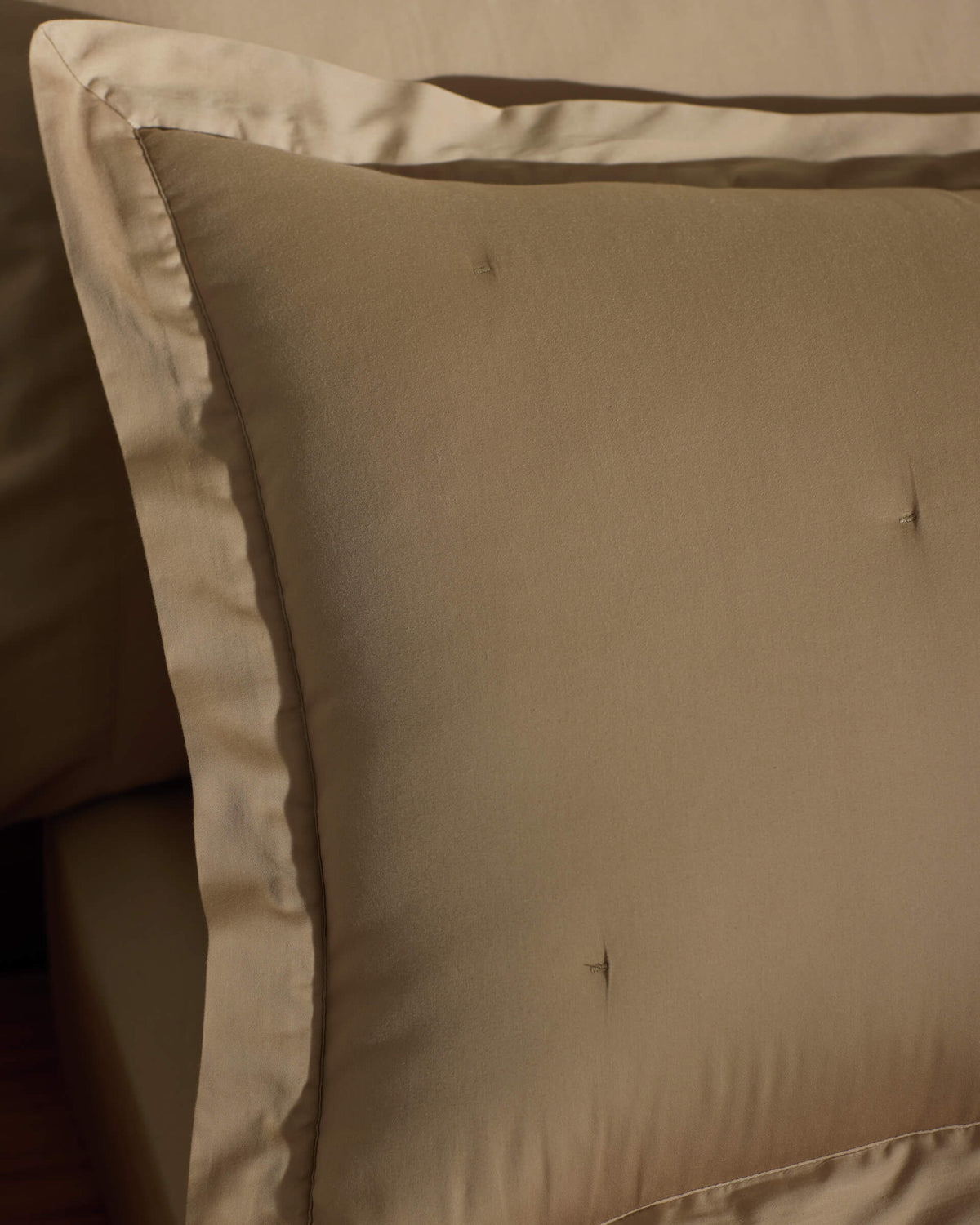 A close-up of a neatly made bed featuring Cozy Earth Soft-Wash Cotton Quilted Shams in beige, showcasing their smooth quilted texture and subtle tufting, complemented by matching beige bedding.|Color:Sandalwood