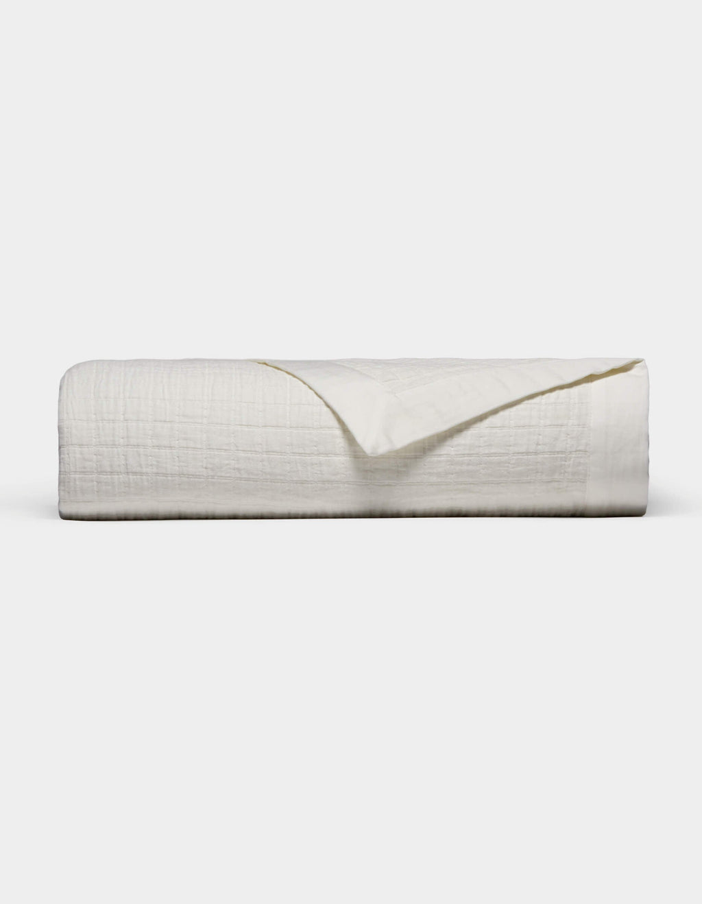 The Waterfront Grid Matelasse Blanket by Cozy Earth is shown neatly folded with a textured, crinkled surface against a plain light background. One corner is flipped over to reveal the underside.|Color:Sea Salt