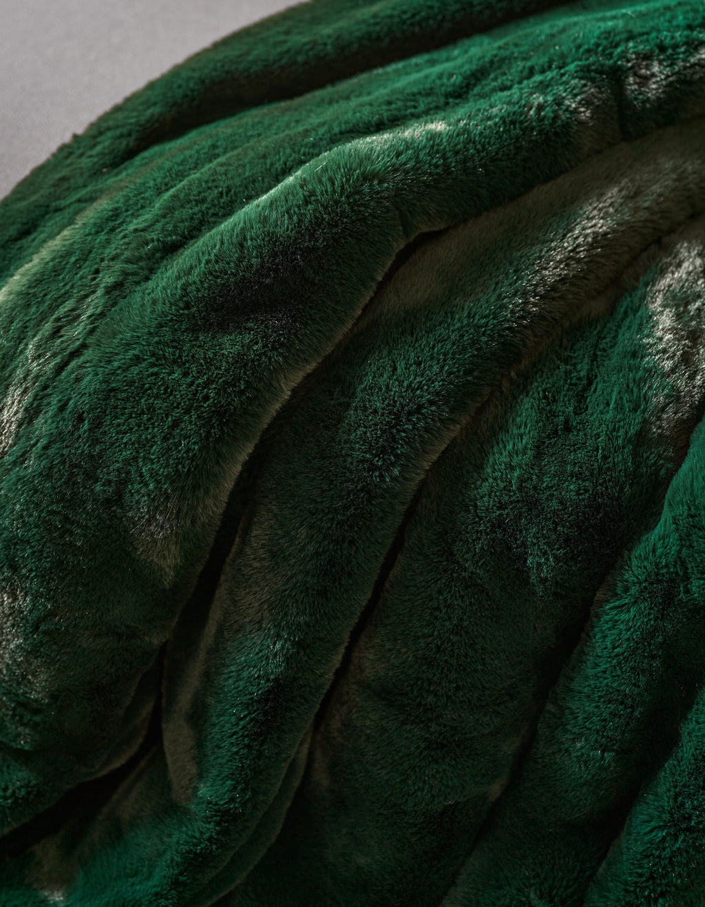 A close-up of the Cozy Earth Channel Cuddle Blanket in plush, dark green faux fur, draped in soft, wavy folds to highlight its velvety texture and elegant sheen.|Color:Emerald
