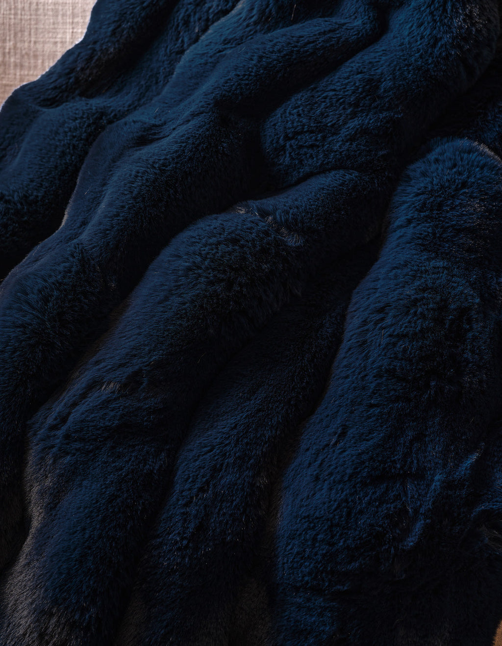 The Double Bubble Cuddle Blanket by Cozy Earth features dark blue faux fur fabric with a soft, plush texture, elegantly arranged in gentle, wavy folds.|Color:Eclipse