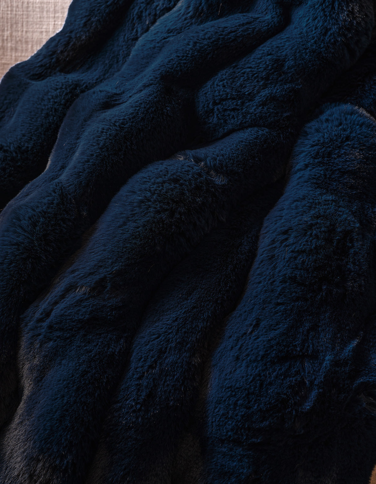 The Double Bubble Cuddle Blanket by Cozy Earth features dark blue faux fur fabric with a soft, plush texture, elegantly arranged in gentle, wavy folds.|Color:Eclipse