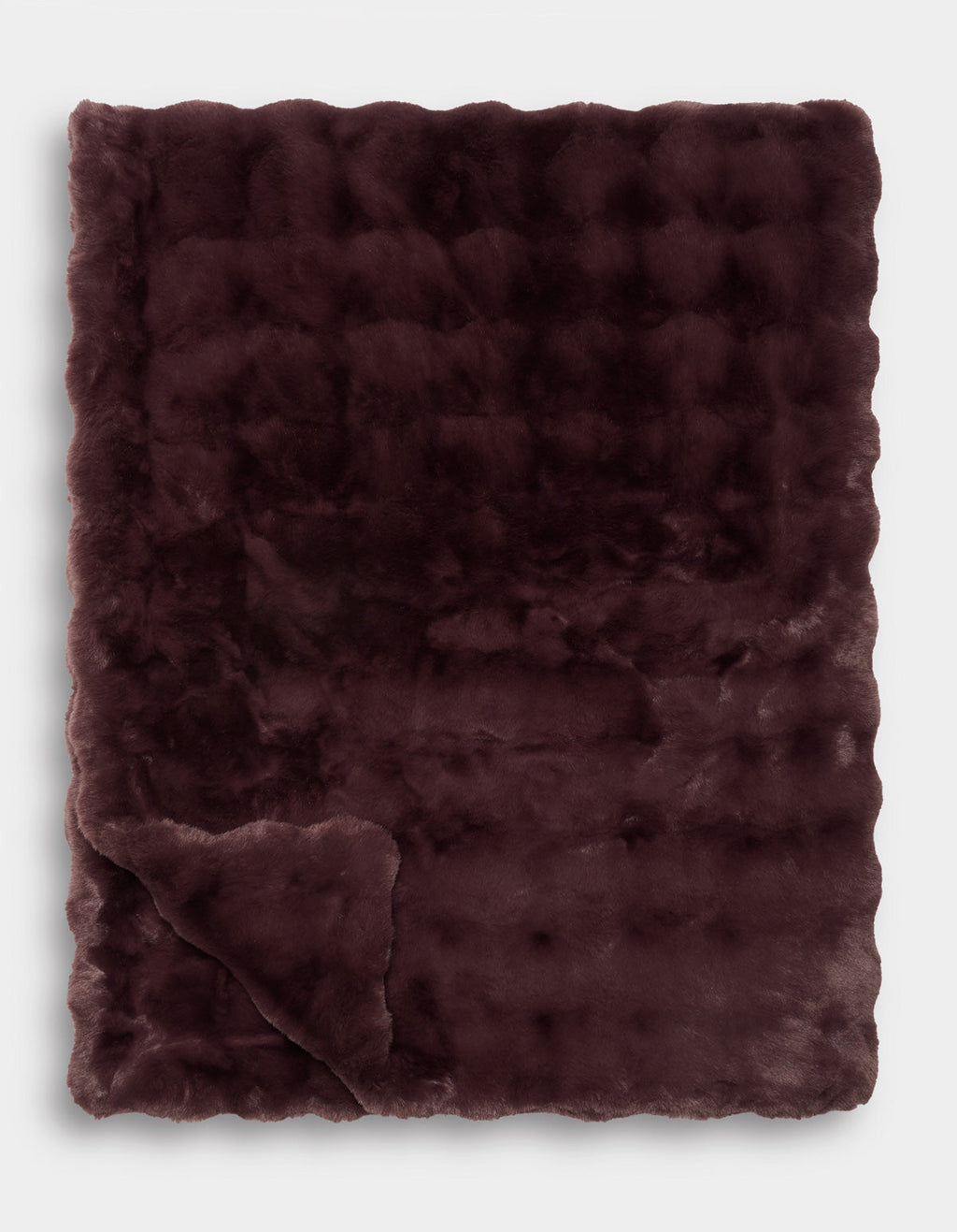 A Bubble Cuddle Blanket by Cozy Earth is displayed folded with one corner turned up, revealing its soft texture and subtle checkered pattern.|Color:Raisin