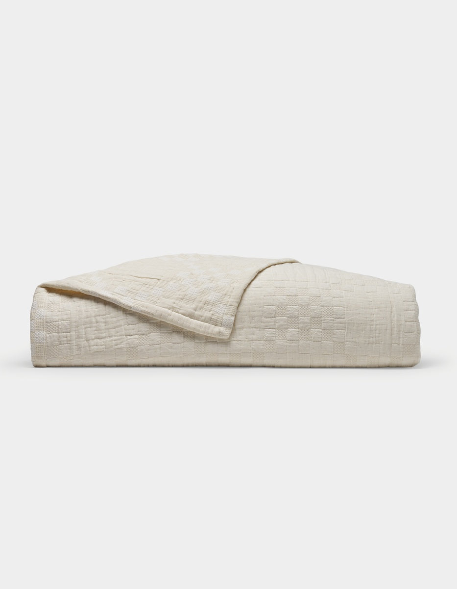 The Sonoma Stitch Quilt by Cozy Earth is a neatly folded, cream-colored quilt featuring a subtle checkered pattern and displayed on a plain white background.|Color:Vintage White