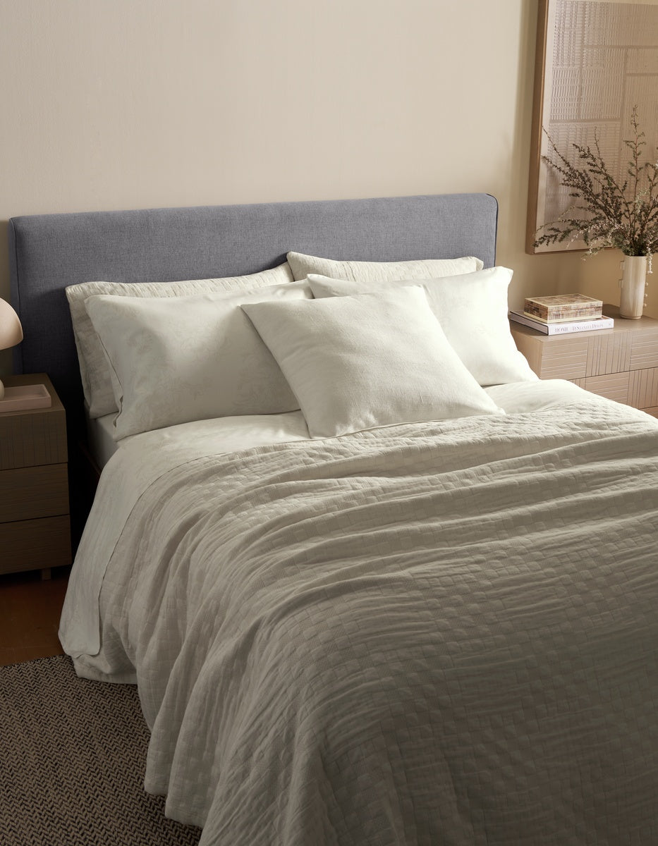 A modern bedroom with a neatly made bed featuring white bedding and pillows, including the Sonoma Throw Pillow by Cozy Earth, a gray upholstered headboard, and light wood nightstands with a vase of greenery.|Color:Sea Salt|Size:24" x 24"
