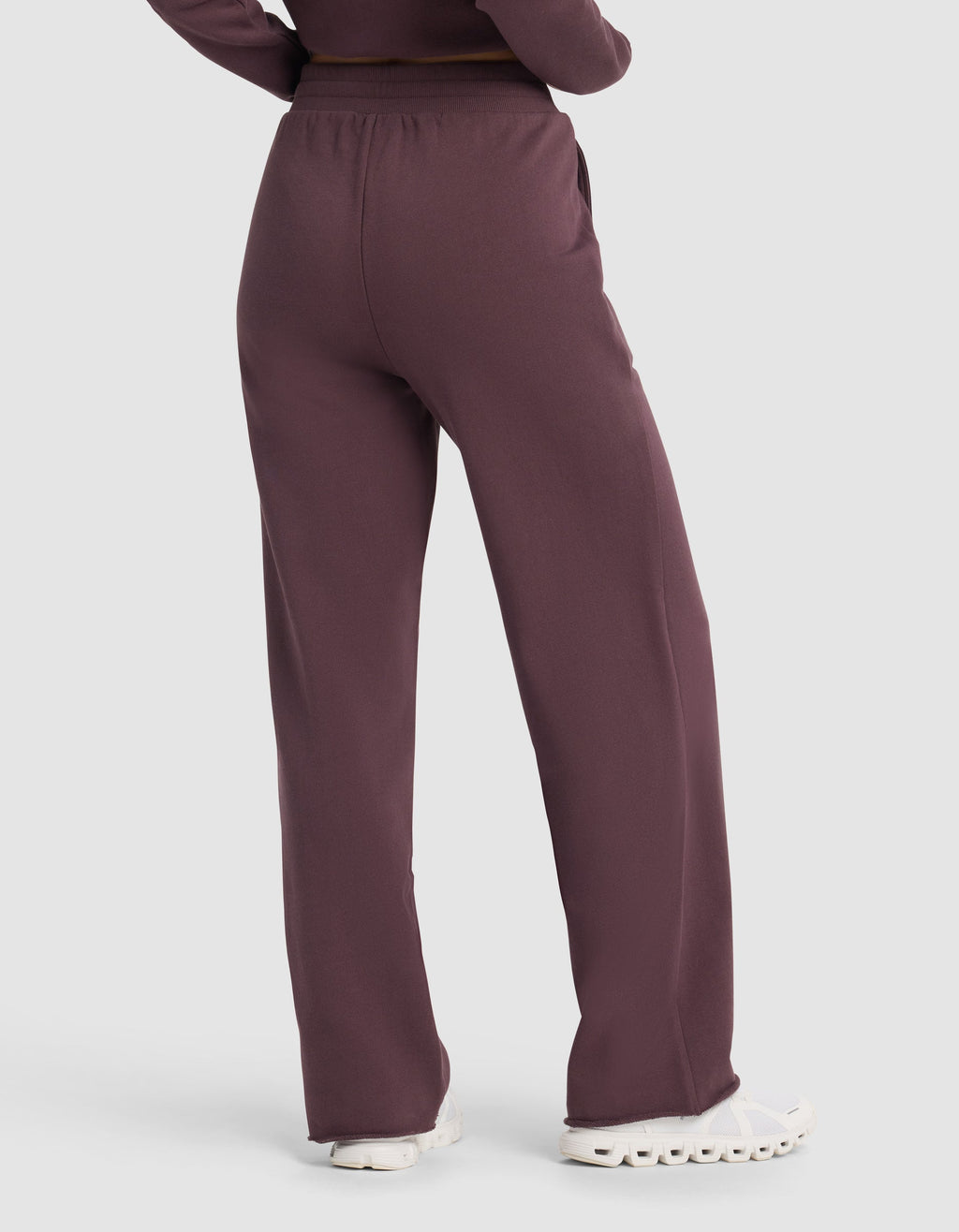 A person is shown from the back wearing Cozy Earth's Chelsea Pant in maroon, a loose-fitting, high-waisted style, paired with white sneakers and arms at their sides.|Color:Fig