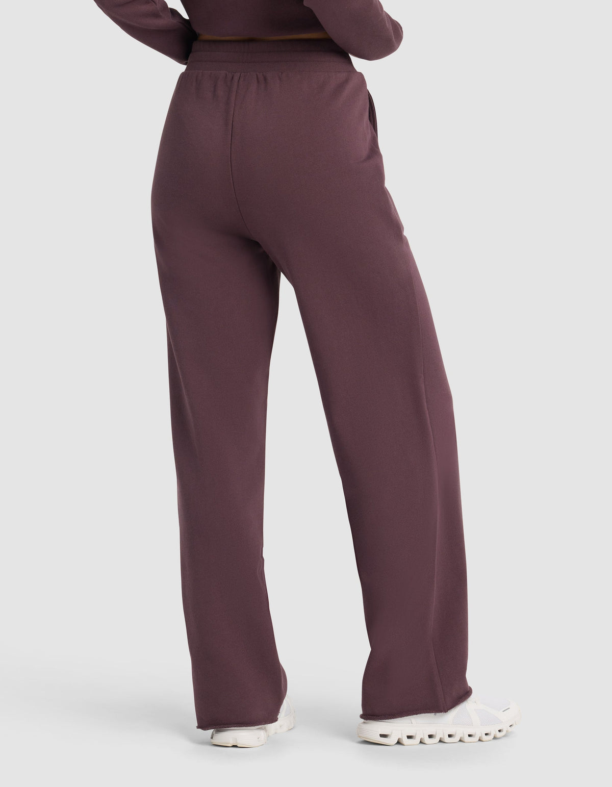 A person is shown from the back wearing Cozy Earth's Chelsea Pant in maroon, a loose-fitting, high-waisted style, paired with white sneakers and arms at their sides.|Color:Fig