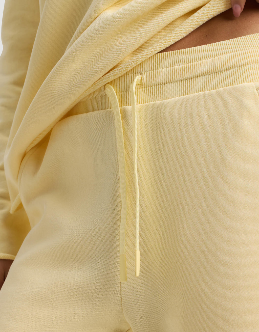 Close-up of a person wearing the Women's Chelsea Cropped Pant by Cozy Earth in light yellow, featuring a matching drawstring and paired with a yellow sweatshirt slightly lifted to reveal the waistband.|Color:Meringue