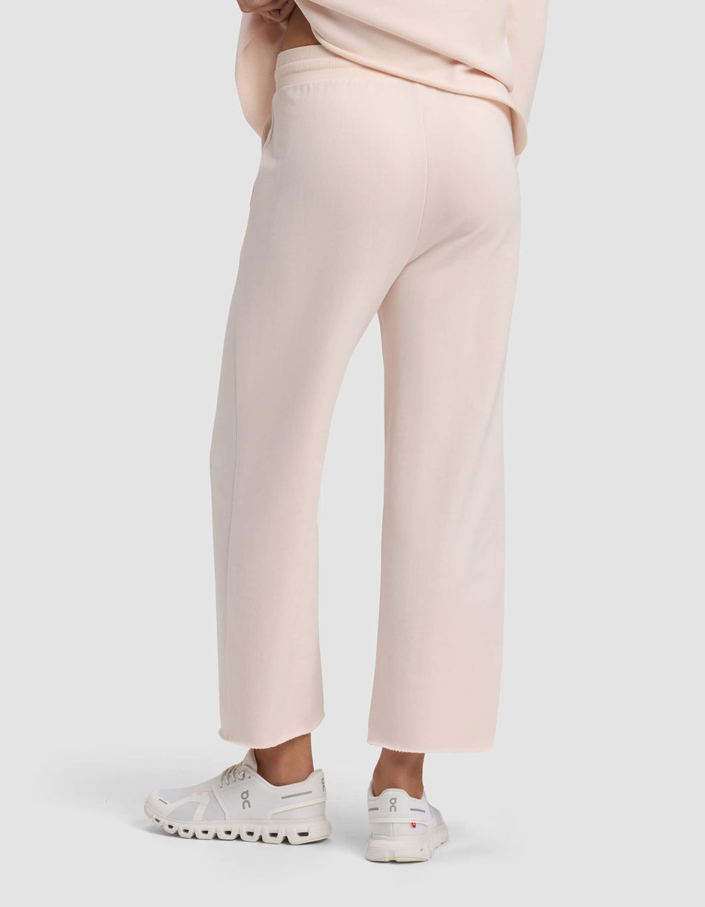 A person is shown from the waist down, facing away, wearing Cozy Earth Women's Chelsea Cropped Pant in light pink and white athletic shoes against a plain light background.|Color:Petal