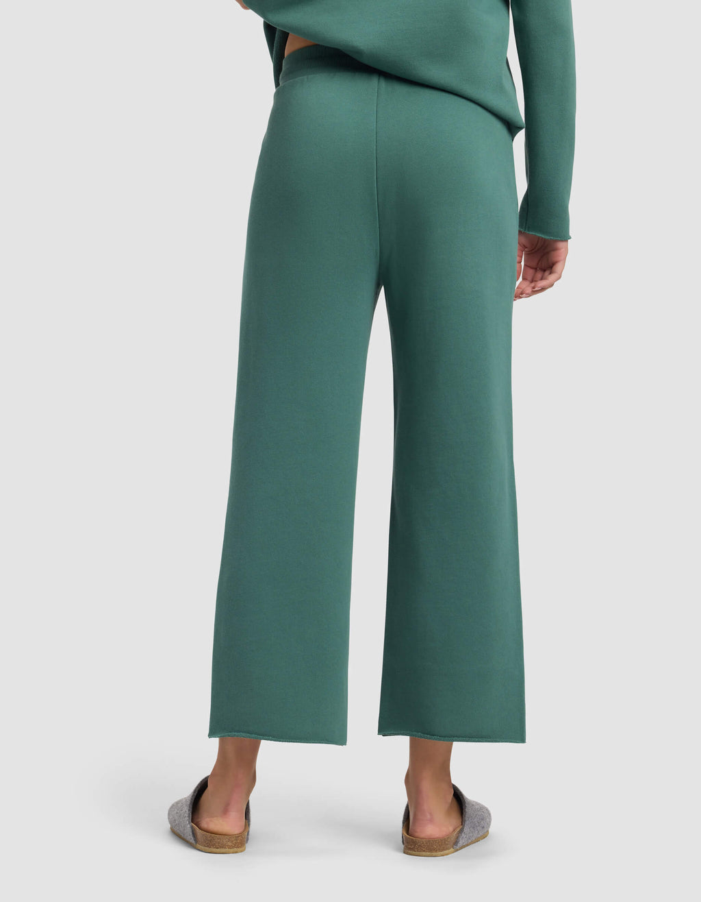 A person is shown from the back wearing Cozy Earth’s Women's Chelsea Cropped Pant in green with a matching top and gray slippers, standing against a plain light background.|Color:Sea Green