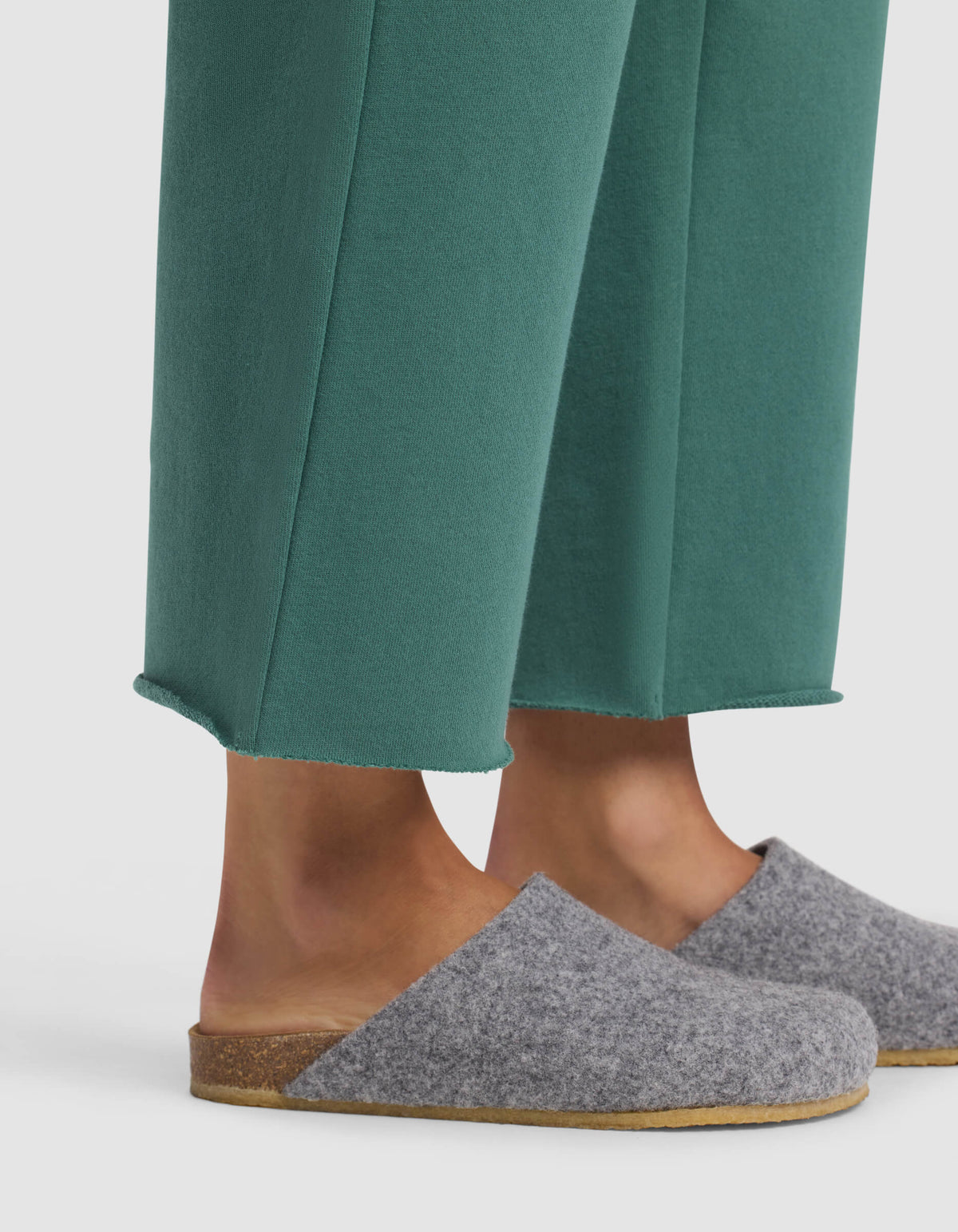 A person wearing Cozy Earth's Women's Chelsea Cropped Pant in green and gray wool slip-on slippers with cork soles, standing against a white background.|Color:Sea Green