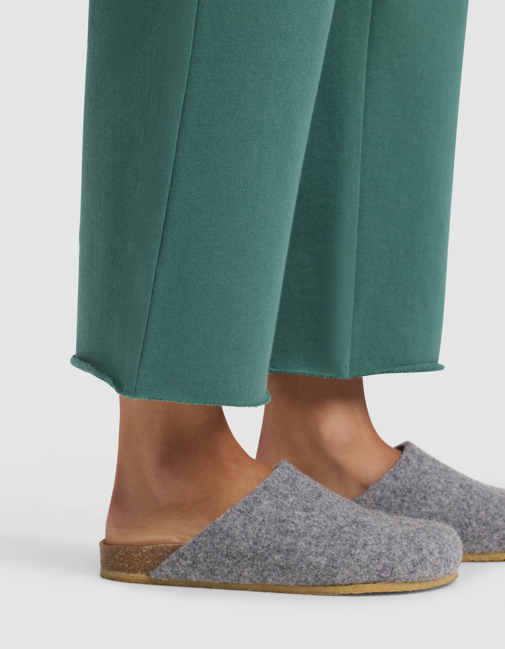 A person wearing Cozy Earth's Women's Chelsea Cropped Pant in green and gray wool slip-on slippers with cork soles, standing against a white background.|Color:Sea Green