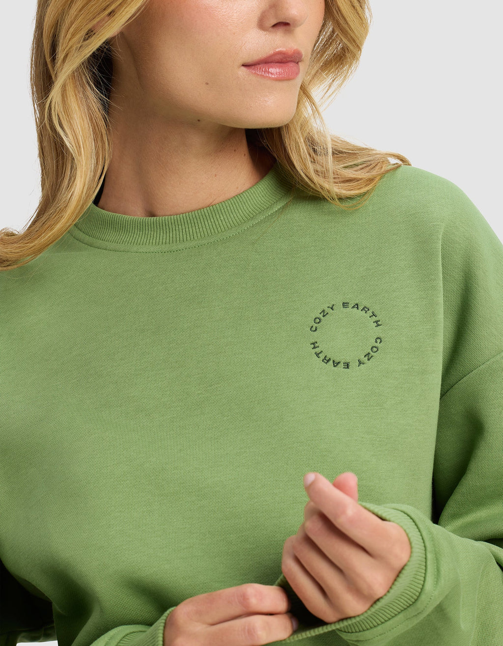 A woman wearing the Cozy Earth Women's Cityscape Crewneck in light green poses against a plain background, facing slightly to the side with her hand near her collar.|Color:Clover