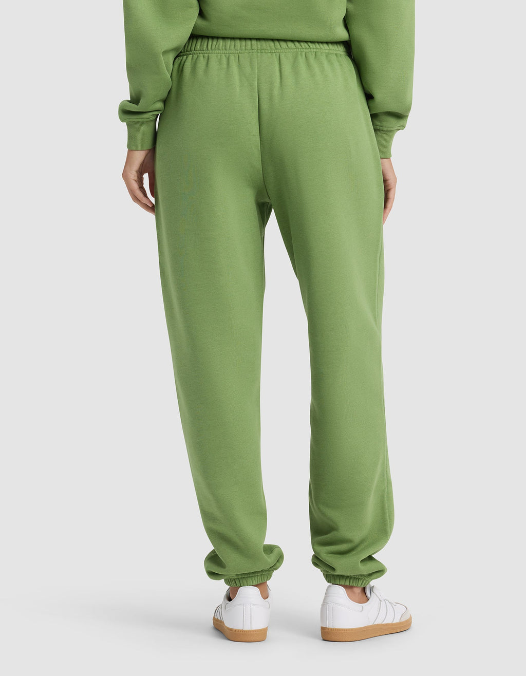 A woman is seen from behind in Cozy Earth's Women's Cityscape Sweatpant and a matching green sweatshirt, paired with white sneakers, against a plain background.|Color:Clover