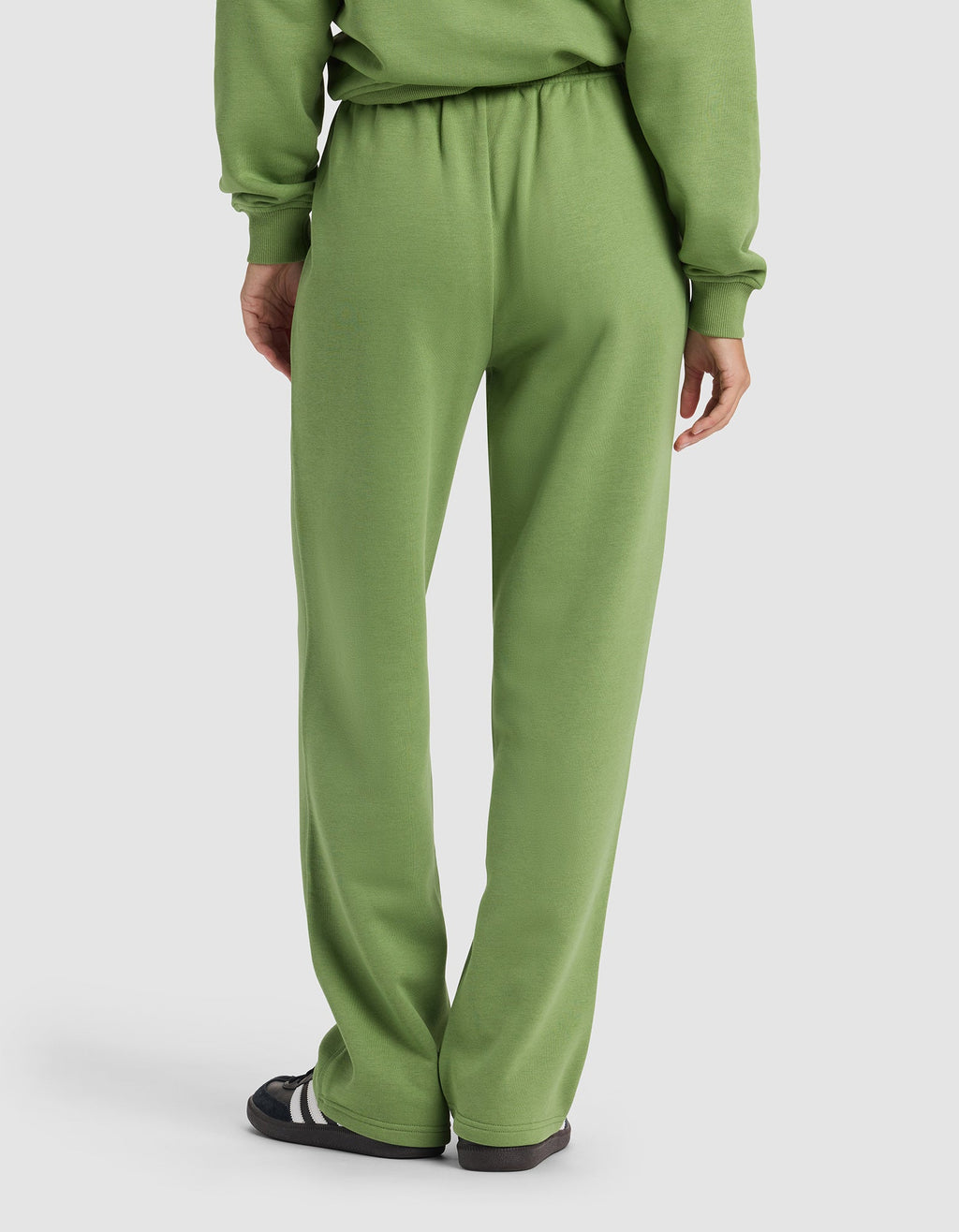 A person is seen from the back wearing the Cozy Earth Women's Cityscape Wide Leg Pant in light green with a matching sweatshirt and black sandals with white stripes, set against a plain, light-colored background.|Color:Clover