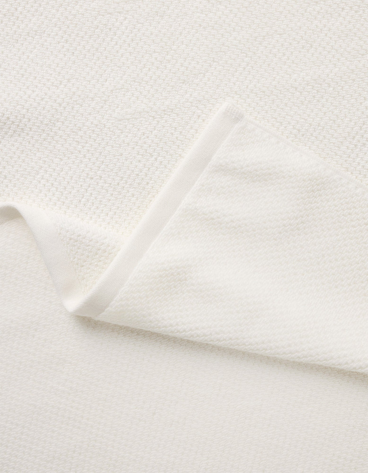 A close-up of the Nantucket Bath Towel Set by Cozy Earth shows its soft, white textured fabric, with a folded corner revealing the towel’s thickness and elegant woven pattern.|Color:White