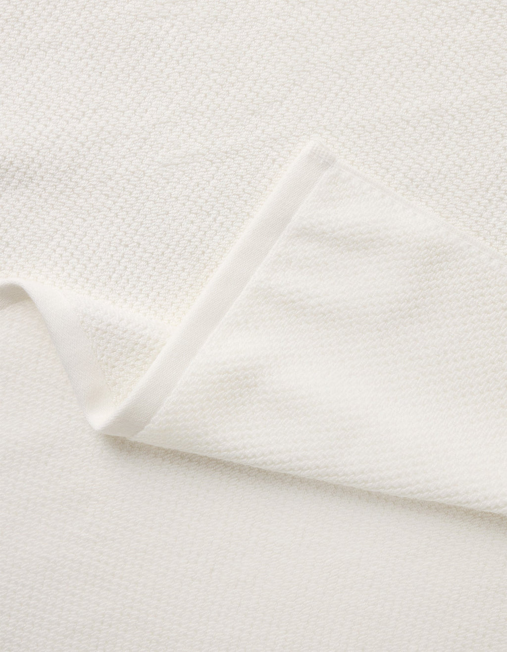 A close-up of the Nantucket Bath Towel Set by Cozy Earth shows its soft, white textured fabric, with a folded corner revealing the towel’s thickness and elegant woven pattern.|Color:White