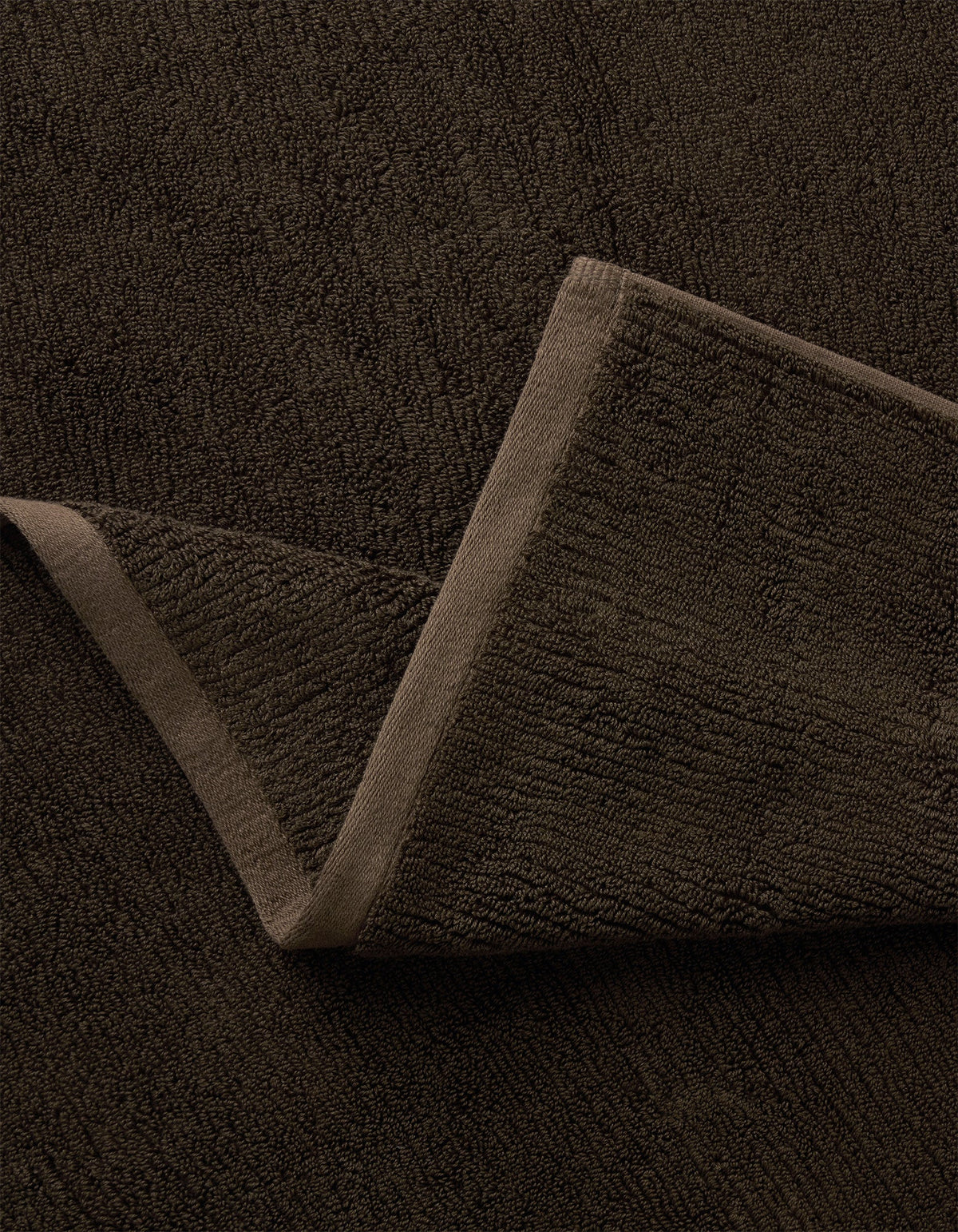 A close-up of the Complete Ribbed Terry Bath Bundle by Cozy Earth in dark brown, featuring one corner folded to reveal its soft ribbed fabric and stitched edges.|Color:Espresso