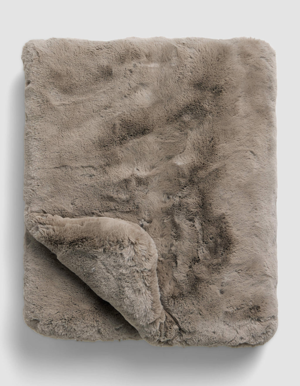 The Superplush Cuddle Blanket by Cozy Earth is a soft, light brown faux fur blanket with a plush texture, shown folded on a plain light gray background. A corner is turned up to reveal its fluffy underside.|Color:Walnut