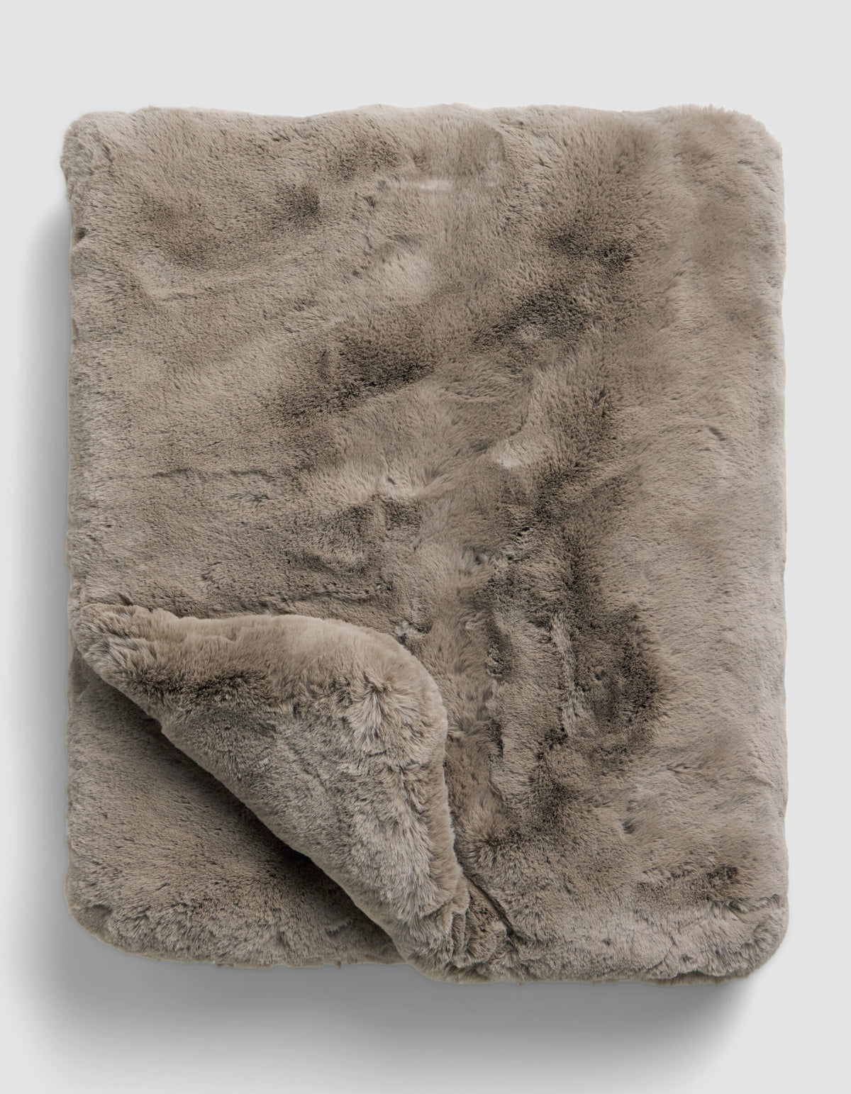 The Superplush Cuddle Blanket by Cozy Earth is a soft, light brown faux fur blanket with a plush texture, shown folded on a plain light gray background. A corner is turned up to reveal its fluffy underside.|Color:Walnut