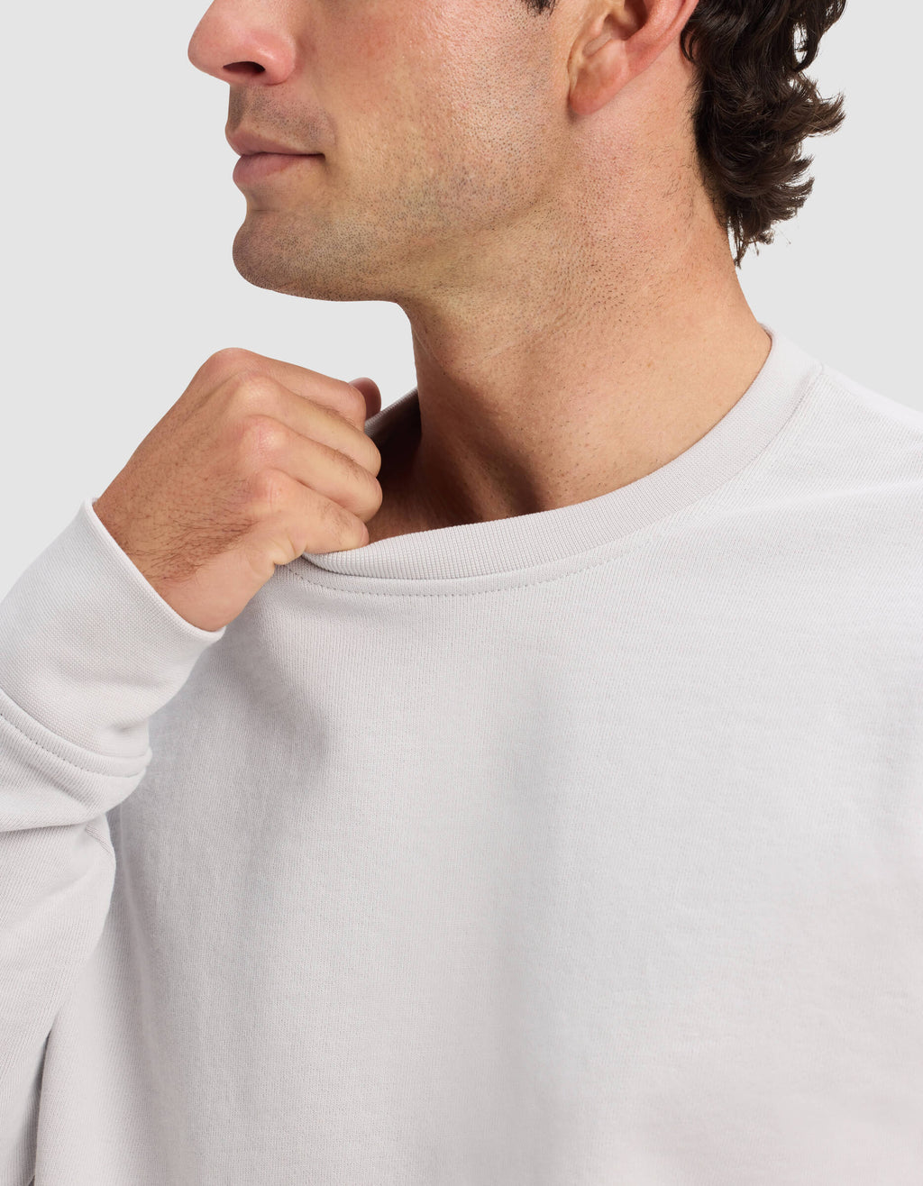A man wears the Cozy Earth Men's Dylan Crewneck, gently pulling the collar away from his neck with his right hand. Only his lower face and upper torso appear against a plain background.|Color:Dew