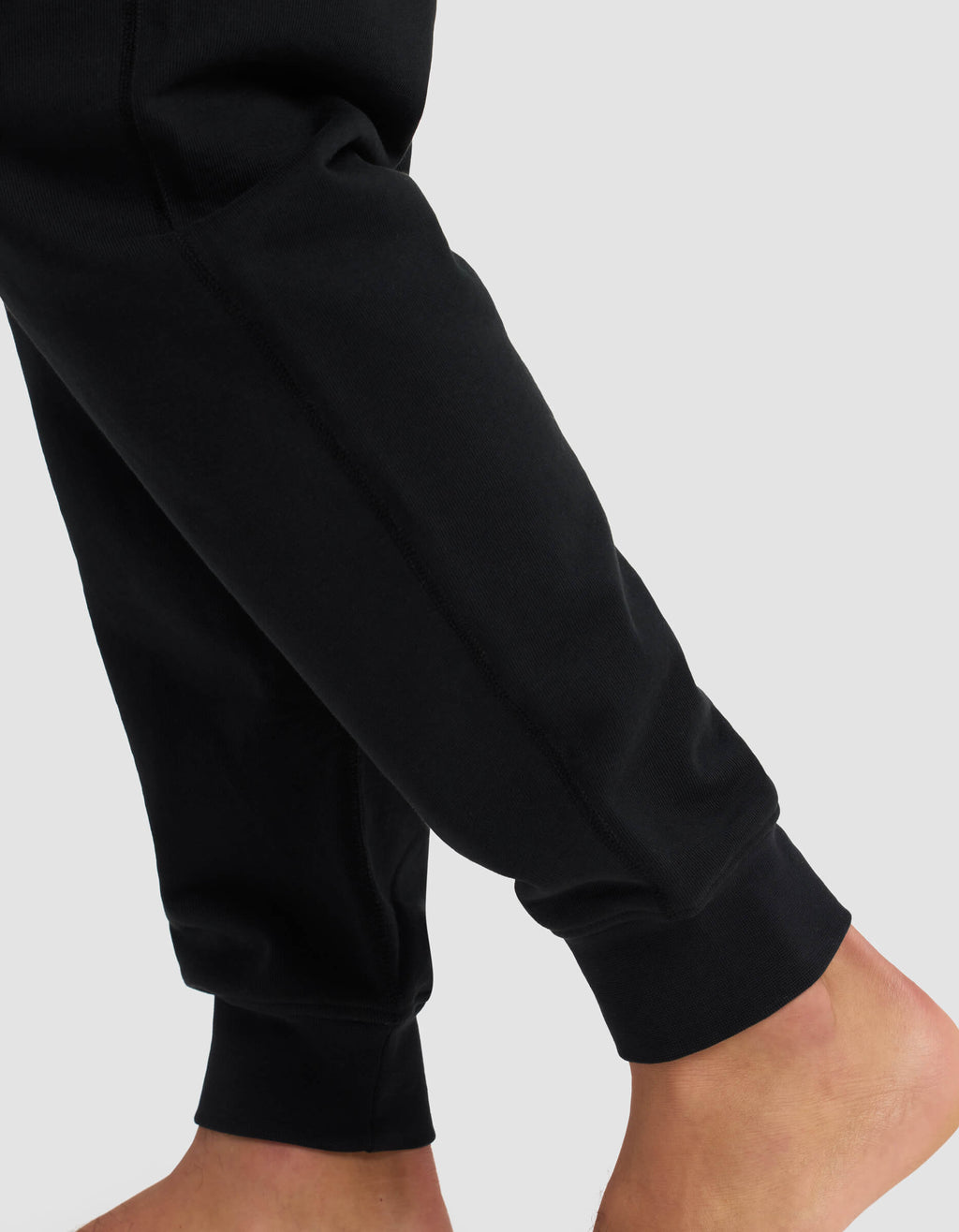 A close-up shows a person standing barefoot in Cozy Earth's Men's Dylan Jogger with ribbed cuffs, against a plain light gray background.|Color:Jet Black