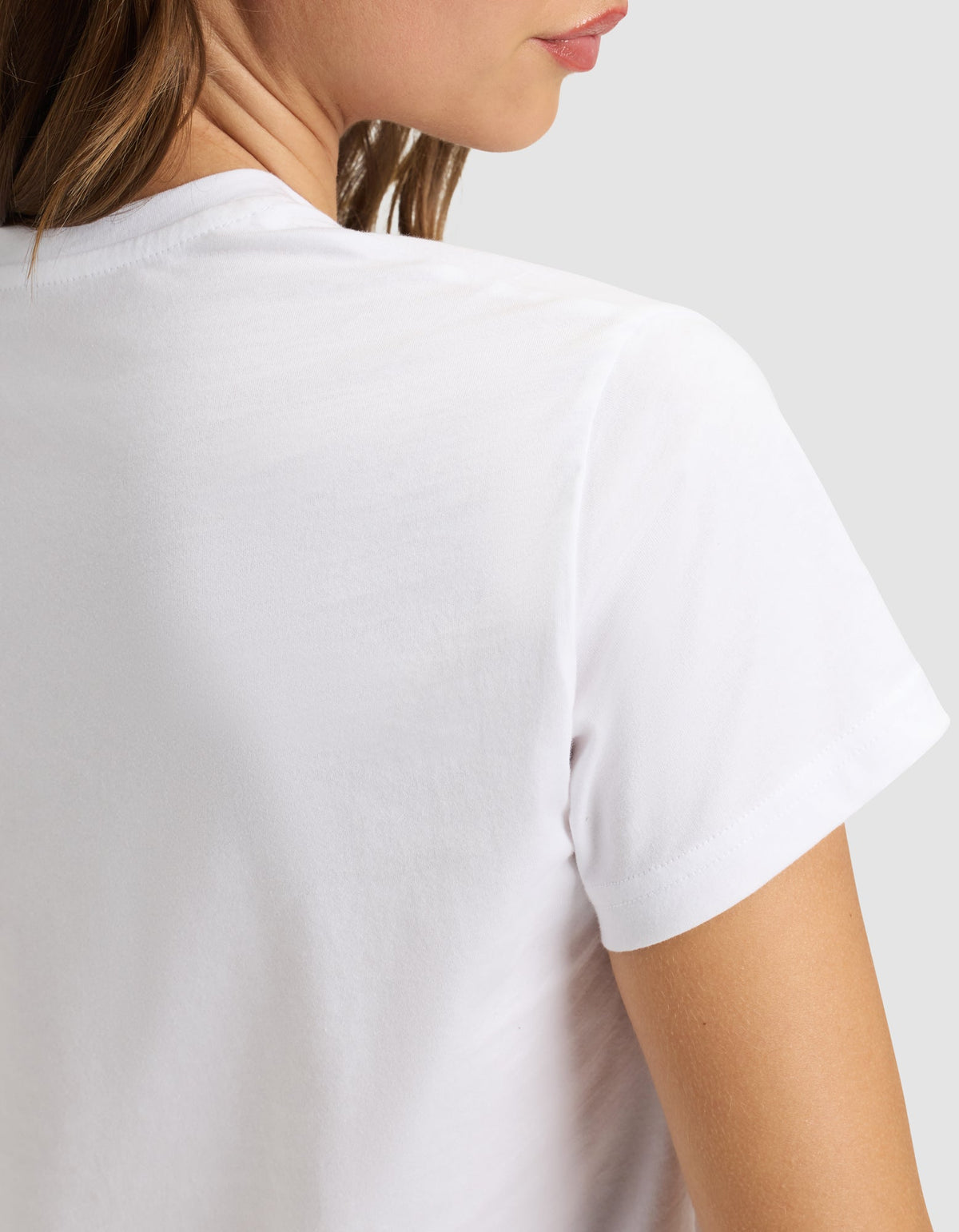 A woman wears the Cozy Earth Women's Easy Tee, shown from the back and slightly to the side, with part of her face, neck, and shoulder visible against a plain light background. |Color:White