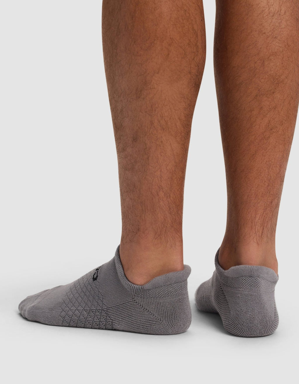 Back view of a person wearing Cozy Earth Essential Ankle Socks, low-cut gray socks that barely cover the ankles, standing on a white surface with lower legs visible.|Color:Stone