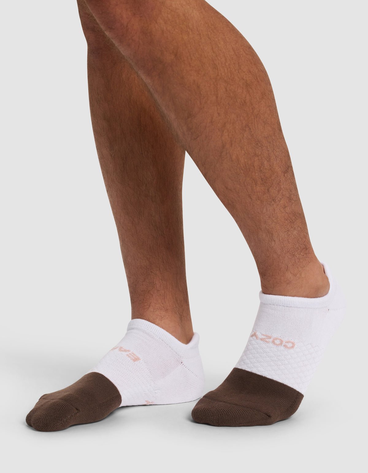 A person wears Cozy Earth Essential Ankle Socks with brown toes, standing on a light grey surface. Only the feet and lower legs are shown.|Color:Cedar