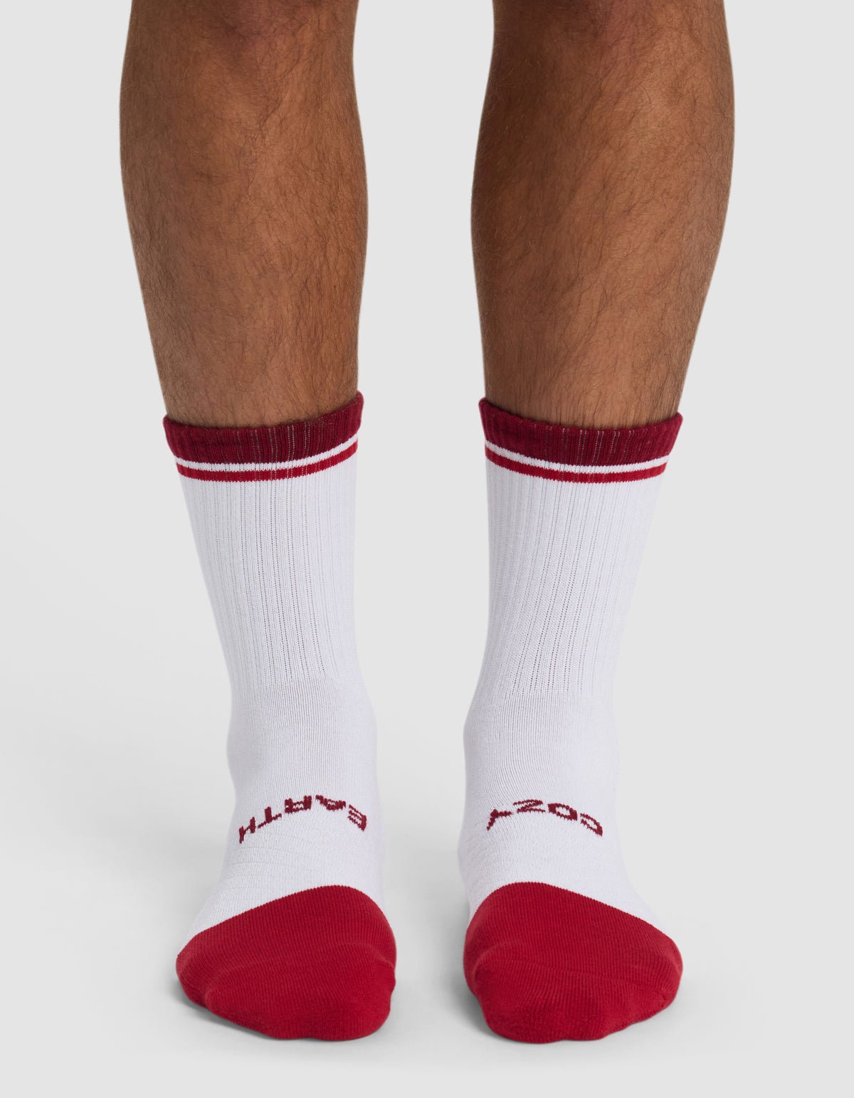 Someone wearing Cozy Earth's Essential Calf Sock in white, featuring red toes, heels, top stripes, and red "EARTH" on the left sock and "COZY" on the right sock near the toes.|Color:Crimson