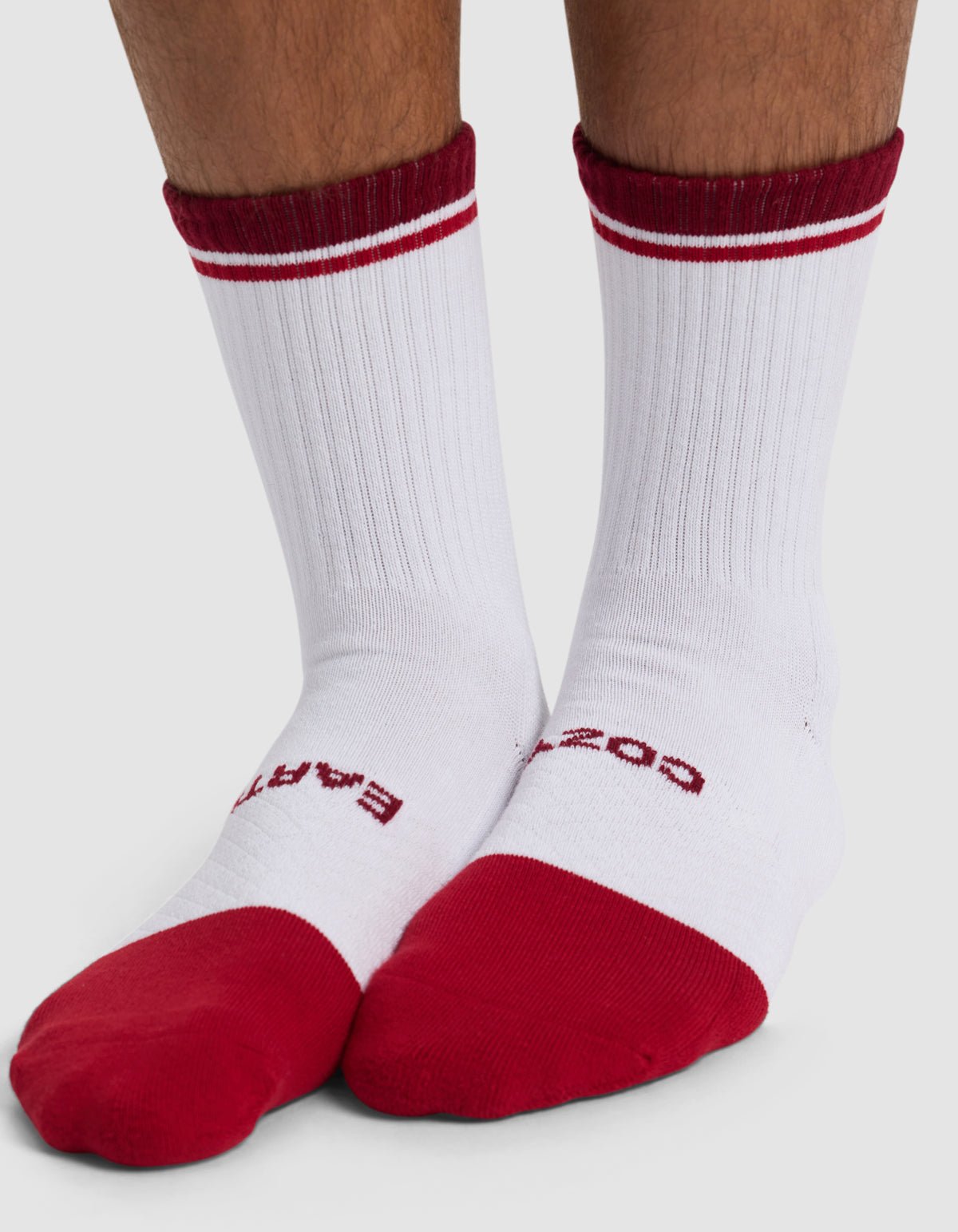 A person wears Cozy Earth's Essential Calf Sock: white crew socks with red toes, heels, cuffs, two red stripes on the cuffs, and red text on the top of the feet.|Color:Crimson