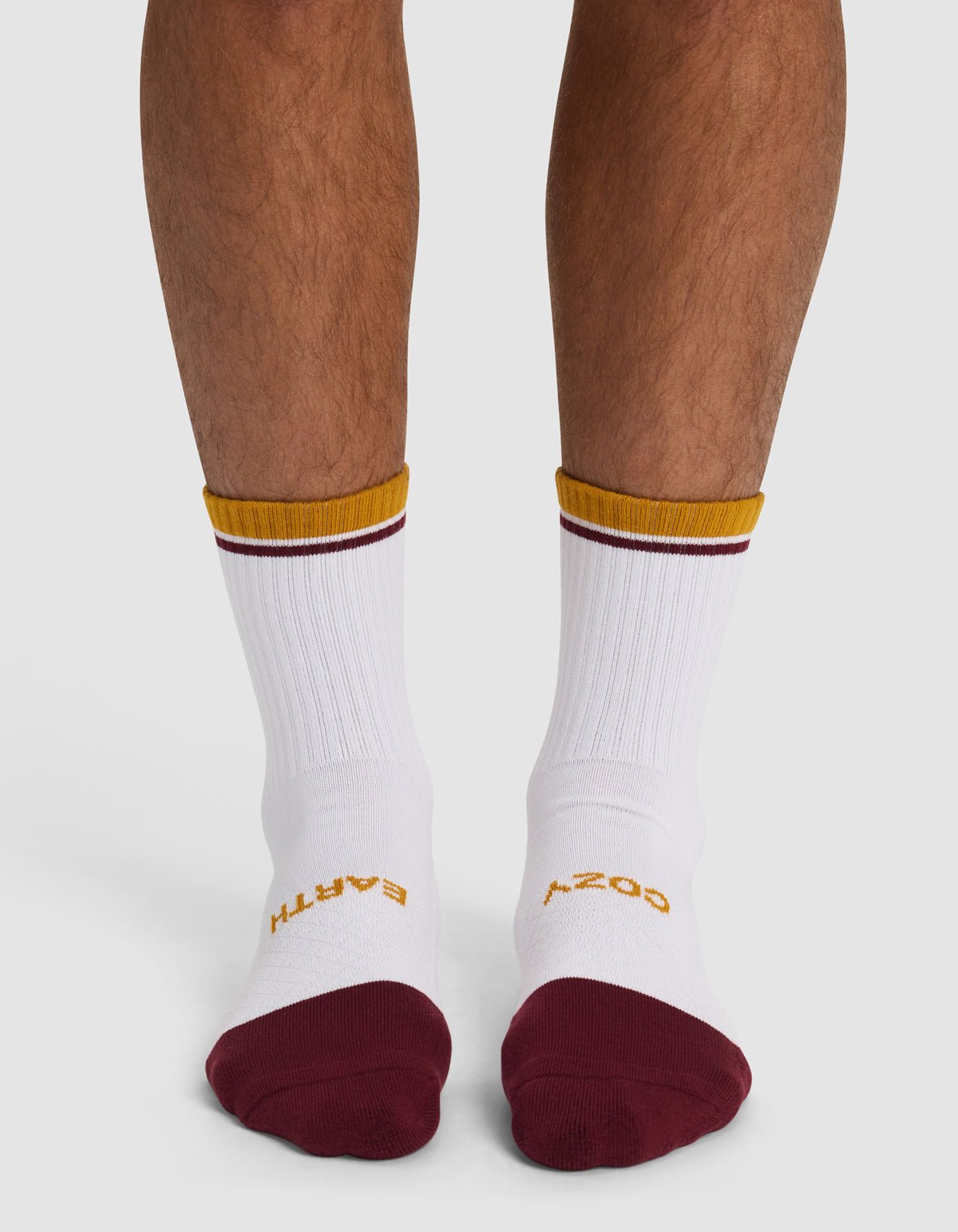 A pair of legs from the knees down wears Cozy Earth Essential Calf Socks—white with maroon toes and gold trim. "EARTH" in gold is on the left sock, "COSY" in gold on the right.|Color:Burgundy