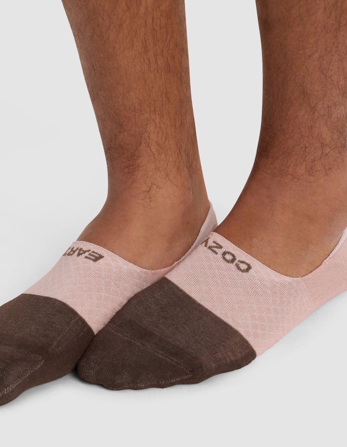 Close-up of a person's lower legs and feet wearing Cozy Earth Essential No-Show Socks in pink and brown with text near the ankle, standing on a light surface.|Color:Cedar