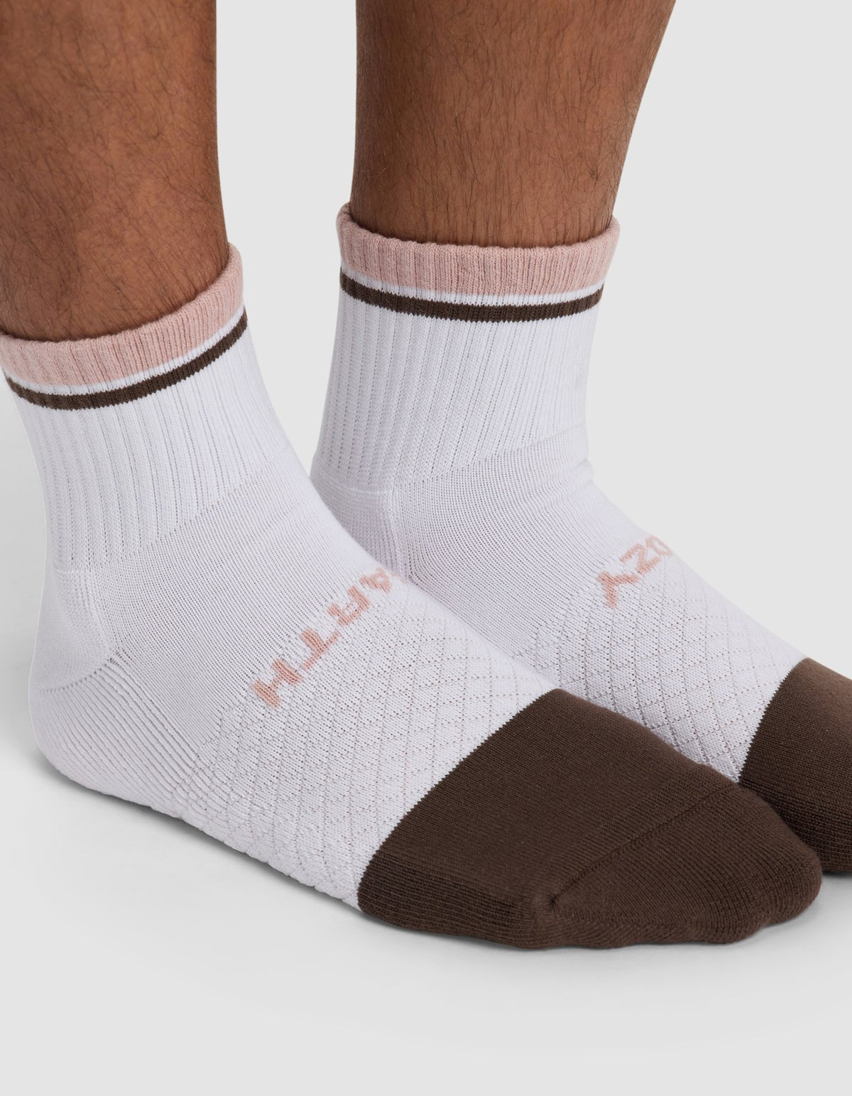 A close-up of feet wearing Cozy Earth's Essential Quarter Socks in white, featuring brown toes and rims with light pink trim near the cuffs. The brand name appears subtly on the sides.|Color:Cedar