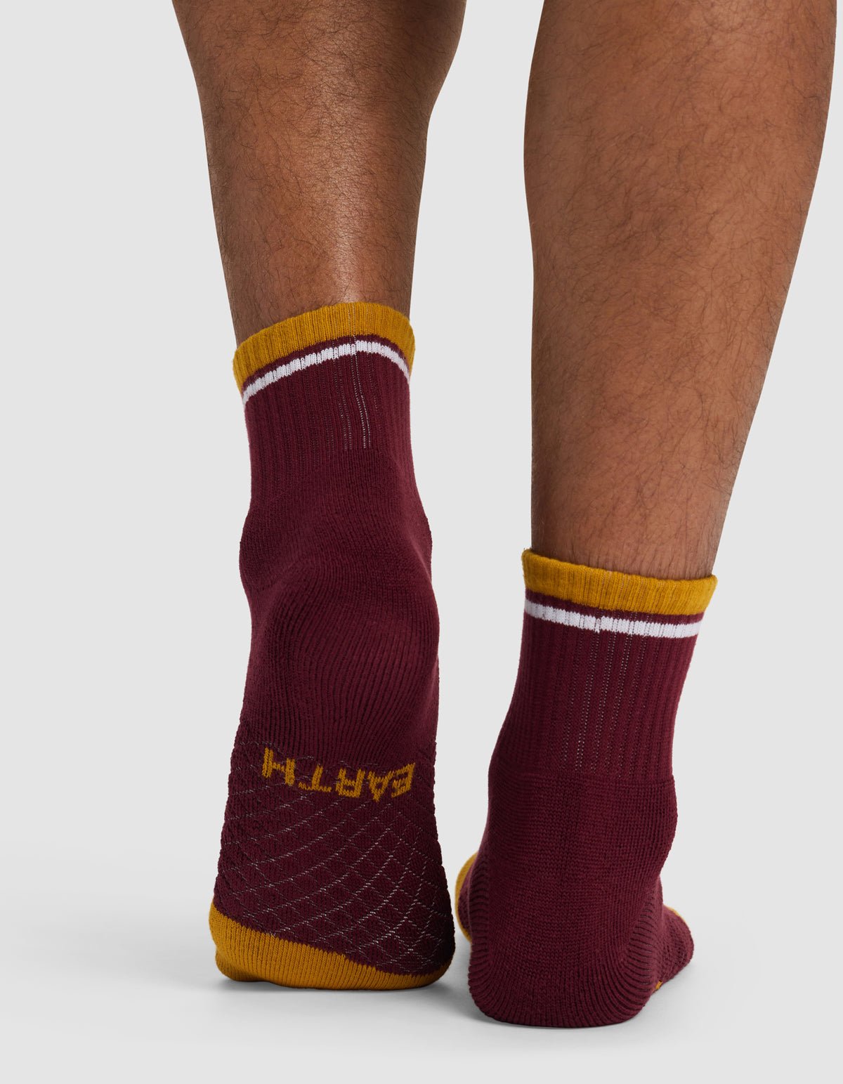 Someone stands on tiptoe wearing Cozy Earth Essential Quarter Socks in maroon with yellow and white trim. The textured grip soles display the word "EARTH" in yellow on one sock.|Color:Burgundy