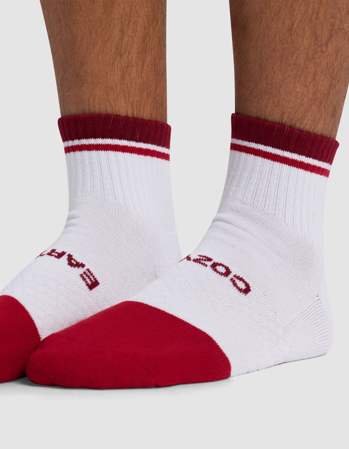 Close-up of feet wearing Cozy Earth Essential Quarter Socks—white with red toes, heels, cuffs, two thin red stripes near the top, and partially visible red text on the upper foot.|Color:Crimson