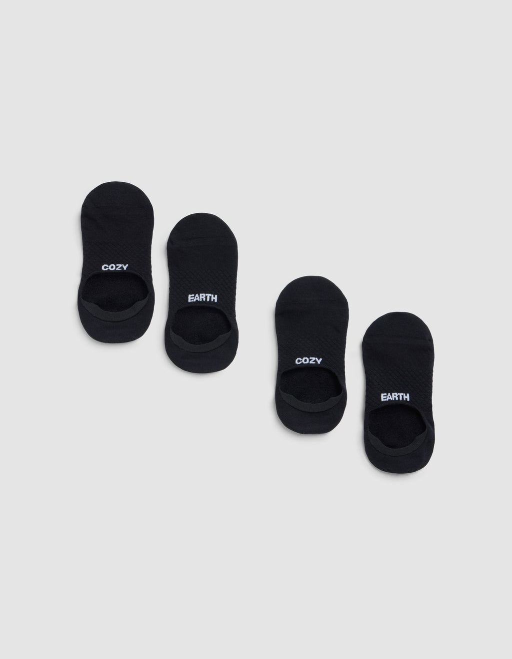 Two pairs of black Essential No-Show Socks by Cozy Earth are displayed on a light gray background. One pair features "COZY" in white lettering, and the other pair displays "EARTH" in white. |Color:Black